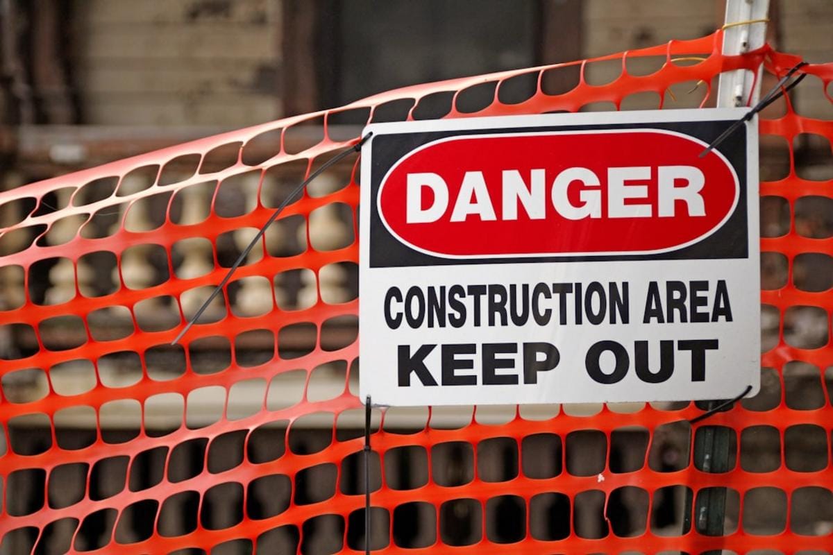 Image of construction workers wearing safety gear on a site with safety signs and equipment
